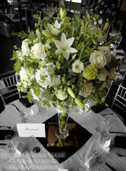 A large flower ball of white and green flowers rests on a tall vase filled 