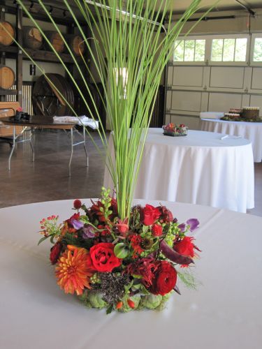 bright orange and red centerpiece with tall grass in artichoke container, George Crest, Françoise Weeks